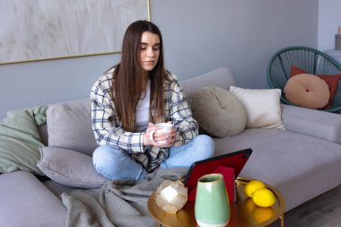 Kafkas kadın serbest çalışan rahat bir koç olarak rahat bir evde oturuyor ve modern tablet üzerinde uzaktan öğreniyor, yetenekli bir kadın internet sitesinde tablet uygulaması üzerinden webinar izliyor..