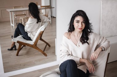 Zarif giysiler içinde genç, gülümseyen bayan girişimci çağdaş iş yerinde oturuyor ve kameraya bakıyor.