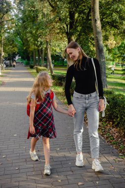 Sevimli küçük kız, annesiyle birlikte okula döndüğü için heyecanlanıyor. Sırt çantalı güzel bir kız annesiyle sokakta yürüyor..