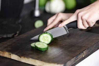 Kadın eli odun keserken salatalık kesiyor.