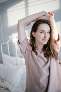 Mutlu, genç, güzel bir kadın ellerini kaldırır, yatak odasındaki yatağın yanında durur. İnsanlar ve Sabah konsepti.