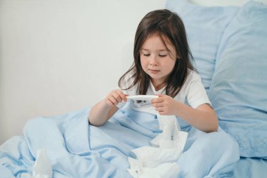 Küçük bir kız ateşini ölçüyor. Çocuk soğuk algınlığına yakalandı ve evde tedavi ediliyor. Üşütmek için yatak istirahati. Çocuklarda mevsimsel soğuk algınlığı.