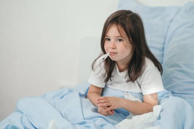 Küçük bir kız ateşini ölçüyor. Çocuk soğuk algınlığına yakalandı ve evde tedavi ediliyor. Üşütmek için yatak istirahati. Çocuklarda mevsimsel soğuk algınlığı