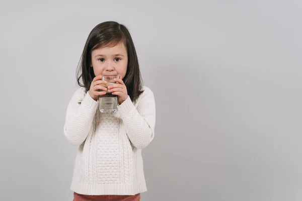 Ребёнок пьёт воду из стакана. Девушка с темными волосами держит стакан воды. Брюнетка ведет здоровый образ жизни — стоковое фото