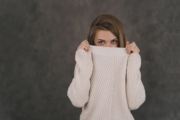 グレーの背景にライトセーターの女の子。少女はセーターの後ろに顔を隠している。少女は目しか見えない — ストック写真