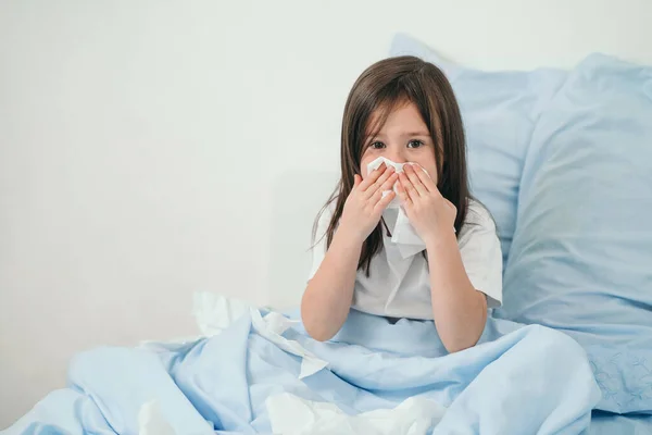 La bambina ha preso il raffreddore. I bambini starnutiscono in un fazzoletto. Il bambino è malato e viene curato a casa. Freddi stagionali nei bambini — Foto Stock