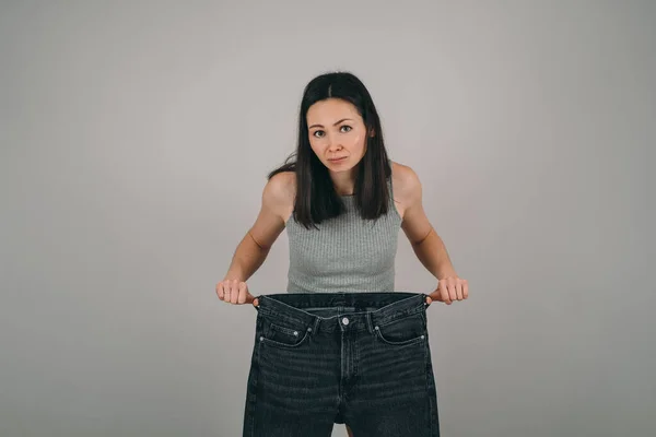 La fille a perdu beaucoup de poids. La fille tient un très gros jean. La femme est surprise de voir comment elle a perdu du poids. Problèmes d'anorexie féminine — Photo