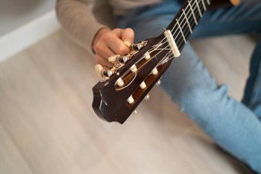 Adam gitarı akort ediyor. Bir gitar fretboard 'unun yakın çekimi. Adam gitar ensesinde akort mandallarını büker.