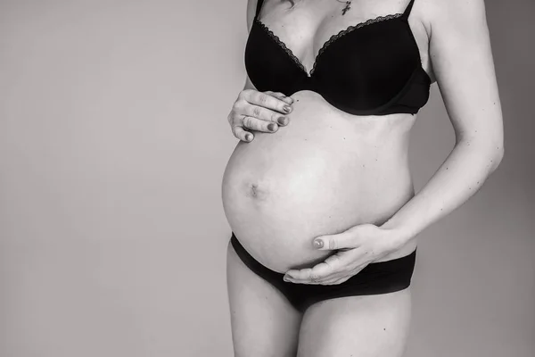 Een zwanger meisje in zwarte lingerie houdt een buik vast. Vrouw wachtend op de geboorte van een kind — Stockfoto