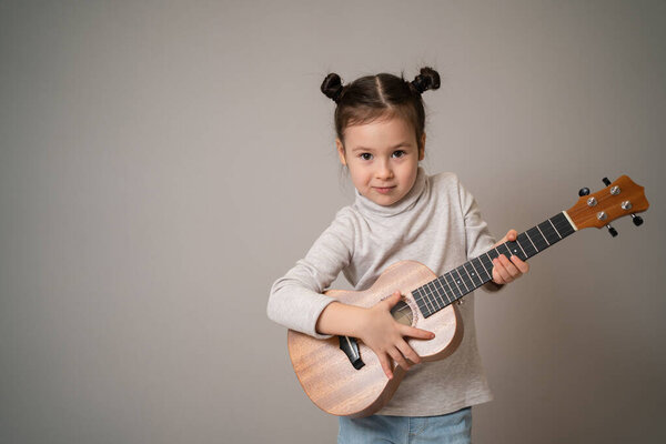 Little girl plays ukulele. Creative development in children. Musical education from childhood. Teaching music online at home.