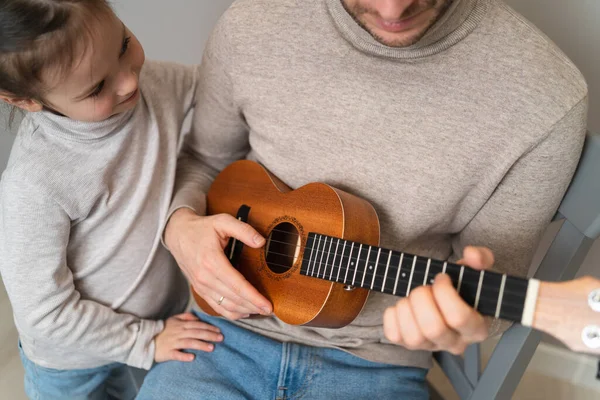 Dad plays the guitar with his daughter. The child learns to play a musical instrument with a tutor. Musical duet of a father with a child