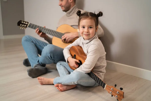 Tata gra na gitarze z córką. Dziecko uczy się grać na instrumencie muzycznym z nauczycielem. Muzyczny duet ojca z dzieckiem — Zdjęcie stockowe