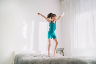 Mutlu çocuk yatakta zıplıyor. Mavi mayo giymiş Avrupalı bir kız atlıyor. Kız ebeveyn yatağında zıplıyor