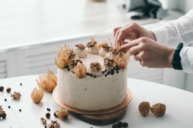 Pasta şefi pastayı fındık ve böğürtlenle süslüyor. Ev yapımı kek. Beyaz bir mutfakta ev yapımı tatlılar yapmak.