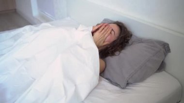 Yatakta güneşli bir sabahın tadını çıkarıyorum. Kız sabah uyanıyor ve esniyor. Yatakta bir kızın uyanışı..