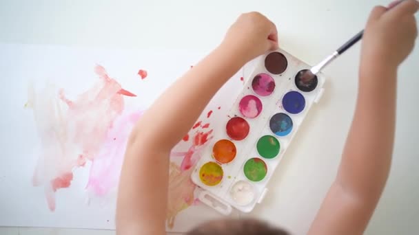 เด็กพยายามที่จะใช้แปรงในสี เด็กเล็กเรียนรู้ที่จะวาดด้วยสีน้ํา มุมมองสูงสุดของกระบวนการสร้างสรรค์ของเด็ก เด็กถาวรพยายามที่จะเรียนรู้ที่จะวาด — วีดีโอสต็อก