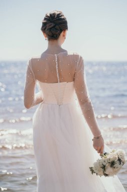 Şık bir gelin arkası dönük durur. Gelinin elinde güzel bir düğün buketi. Güzel ve gür bir gelinlik.. 