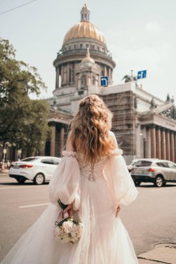 Şık bir gelin arkası dönük durur. Gelinin elinde güzel bir düğün buketi. Güzel ve gür bir gelinlik.. 