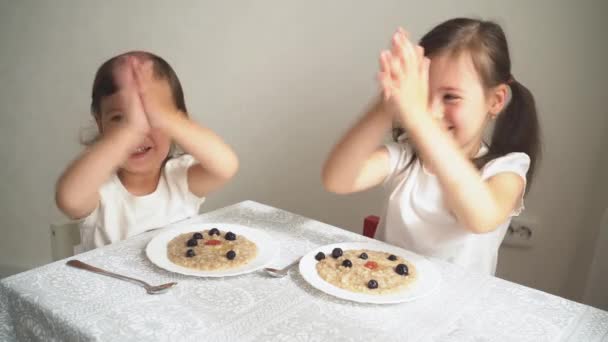 L'enfant mange du porridge avec des baies. Les deux sœurs prennent le petit déjeuner et socialisent. Gros plan enfants heureux à la table. Aliments sains pour les enfants. L'enfant mange du porridge et rit — Video