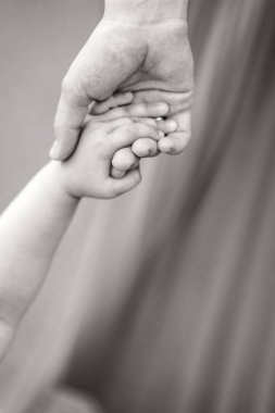 Çocuk annesinin elini sıkıca tutuyor. Çocuğun annesiyle çekilmiş siyah beyaz bir fotoğrafı. Çocuklarına ve ebeveynlerine yakın çekim. Çocuklukla ilgili bir metin için bir yer