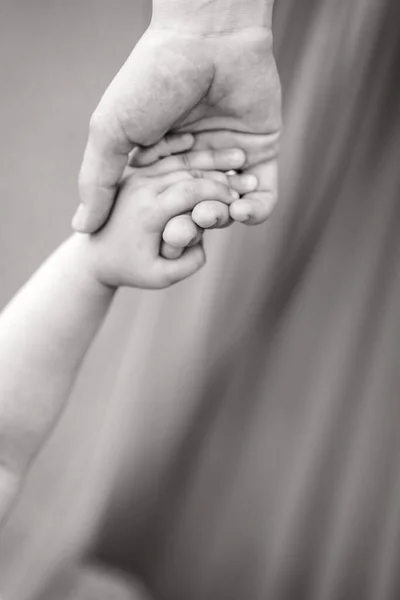 The child holds his mothers hand tightly. Black and white photo of the child with his mother. Close-up of the childs and parents hands. A place for a text about childhood — Stock Photo, Image