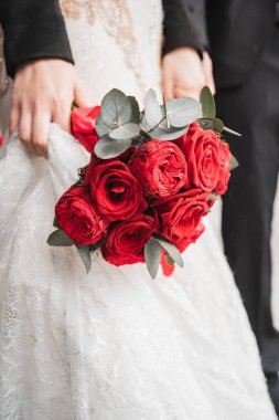 Yakın plan kırmızı düğün buketi. Damat gelinin elini tutar. Bir kızın elinde bir buket gülün dikey fotoğrafı..