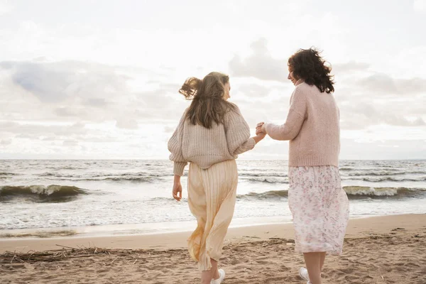 Két nagyon közeli barát sétál a tengerparton. A szerelmes lányok fogják egymás kezét és egymásra néznek. A nővérek szívből beszélnek. Romantikus séta gyönyörű lányok — Stock Fotó