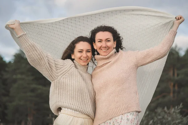 Las dos mujeres más felices disfrutan de la vida y miran a la distancia. Chicas en suéteres ligeros con un tejido de punto grande. Suave y cálido viento sopla sobre las niñas —  Fotos de Stock