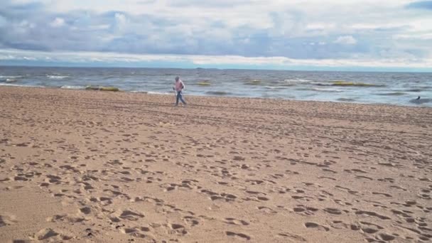 En kvinna är engagerad i nordisk vandring på stranden. En äldre kvinna går längs havet. Vacker himmel med moln över havet — Stockvideo