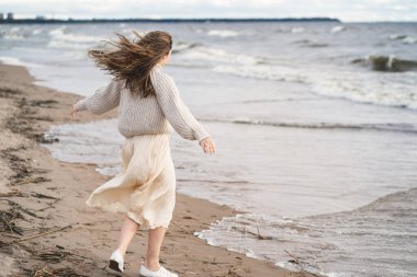Romantik bir kız deniz kenarında rüzgardan hoşlanır. Okyanusta mutlu bir adamın dansı. Hafif elbiseli ve kalın kazaklı bir kadın.