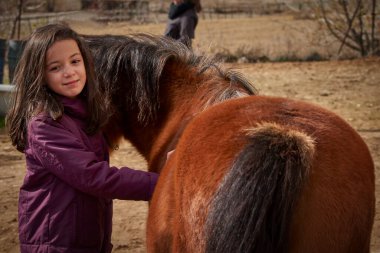 Küçük mutlu kız güzel kahverengi bir atı okşuyor.