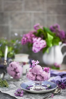 Bir fincan ev yapımı yaban mersinli dondurma ve arka planda leylak.