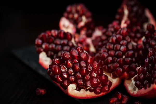 Fresh pomegranate and seeds on black — Stock Photo, Image