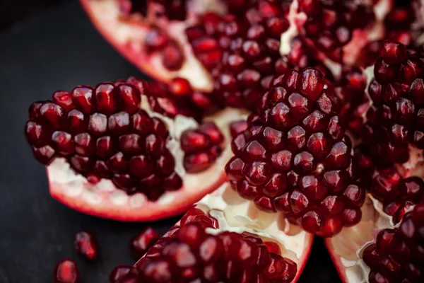 Fresh pomegranate and seeds on black — Stock Photo, Image