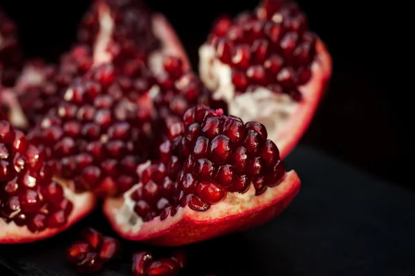 Fresh pomegranate and seeds on black — Stock Photo, Image