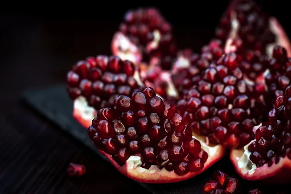 Fresh pomegranate and seeds on black — Stock Photo, Image