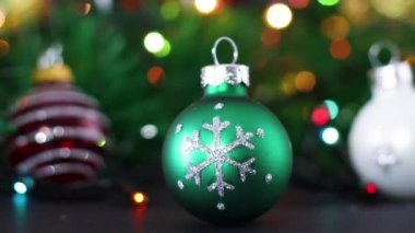 Arkasında yanıp sönen ışıklar olan parlak Noel süslerini kapat. Masada kırmızı yeşil ve beyaz Noel topları