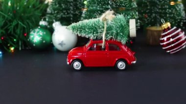 Çatıda Noel ağacı olan klasik kırmızı bir araba ve dekorasyonda yanıp sönen ışıklar.