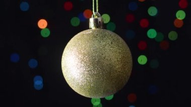 Arkasında yanıp sönen ışıklarla parıldayan altın Noel ağacı sallanıyor.