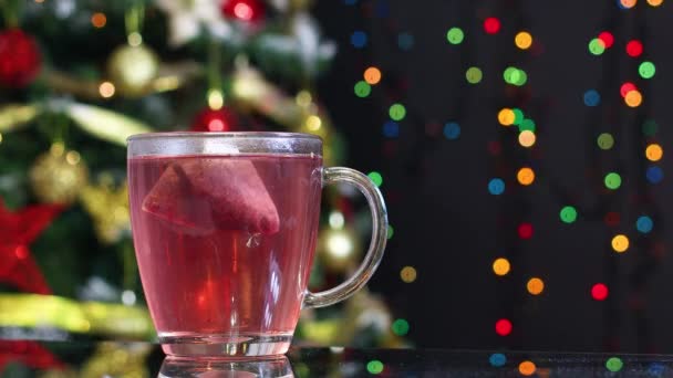 テーブルの上のカップと後ろのクリスマスツリーで熱い赤いお茶 — ストック動画