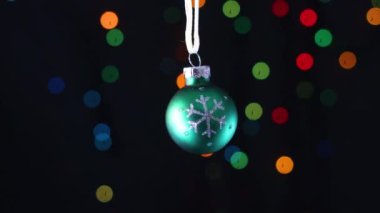 Arkasında yanıp sönen ışıklar olan parıltılı kar tanesi salıncaklı yeşil Noel süsü.