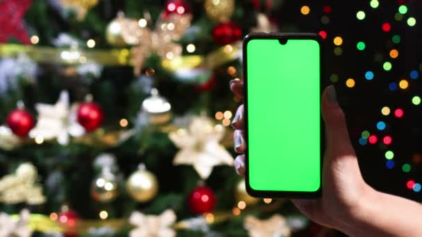 Frauenhand Zeigt Handy Mit Grünem Bildschirm Vor Weihnachtsbaum — Stockvideo