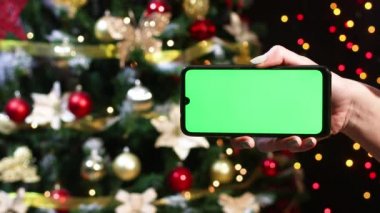 Noel ağacının önündeki yeşil ekranlı modern cep telefonu kadının elinde.
