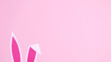 Tavşan kulakları pastel pembe arka planda görünür. Paskalya minimum düz duruş hareketi