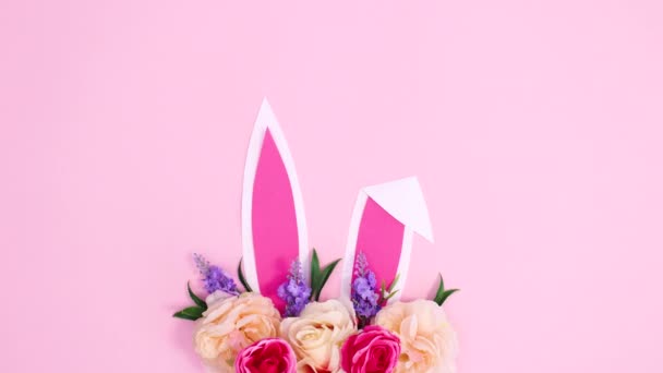 Kreative Osterblütenarrangements mit Hasenohren auf pastellrosa Hintergrund. Flache Laie-Stop-Bewegung