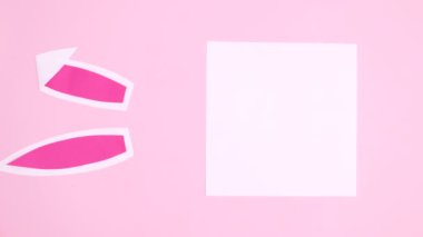 Paskalya için dikey kağıt kart ve tavşan kulakları pastel pembe arka planda görünür. Minimum düz duruş hareketi