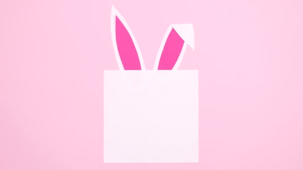 兔子耳朵出现在纸卡片上的粉红背景下 复活节停留时间平铺 — 图库视频影像