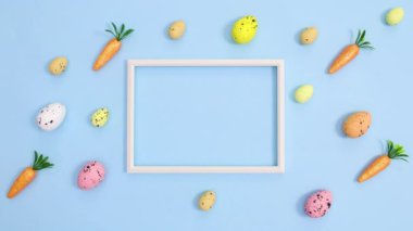 Paskalya yumurtaları ve havuçlar pastel parlak mavi arkaplanda fotokopi çerçevesiyle desen oluşturuyor. Dur hareketi düz yatıyordu