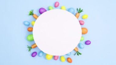 Yaratıcı Paskalya yumurtaları ve havuçlar parlak mavi arka plandaki kağıt kart notlarının altında görünür. Hareket minimumu düz yatar