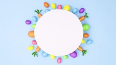 Paskalya canlı yumurtaları ve havuçlar pastel mavi arka planda kağıt kart notlarının etrafında hareket ederler. Minimum düz duruş hareketi